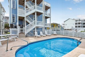 A swimming pool with a white fence, lounge chairs, and a multi-level building with balconies. - Waterview 3BR | Steps to Beach with Pool (Carolina Beach)