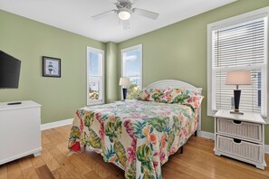 Une chambre à coucher comprenant un lit, une table de chevet, une lampe, un téléviseur et un ventilateur de plafond.