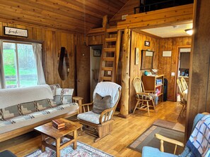 A cozy cabin interior with a wooden floor, a sofa, a rocking chair, a small table, and a ladder. -  Beach cabin in Yachats perfect for relaxing getaways (Yachats)
