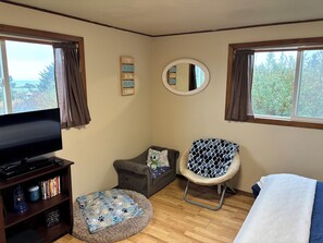 A cozy room with a TV, a pet bed, a chair, and a bed. -  Beach cabin in Yachats perfect for relaxing getaways (Yachats)