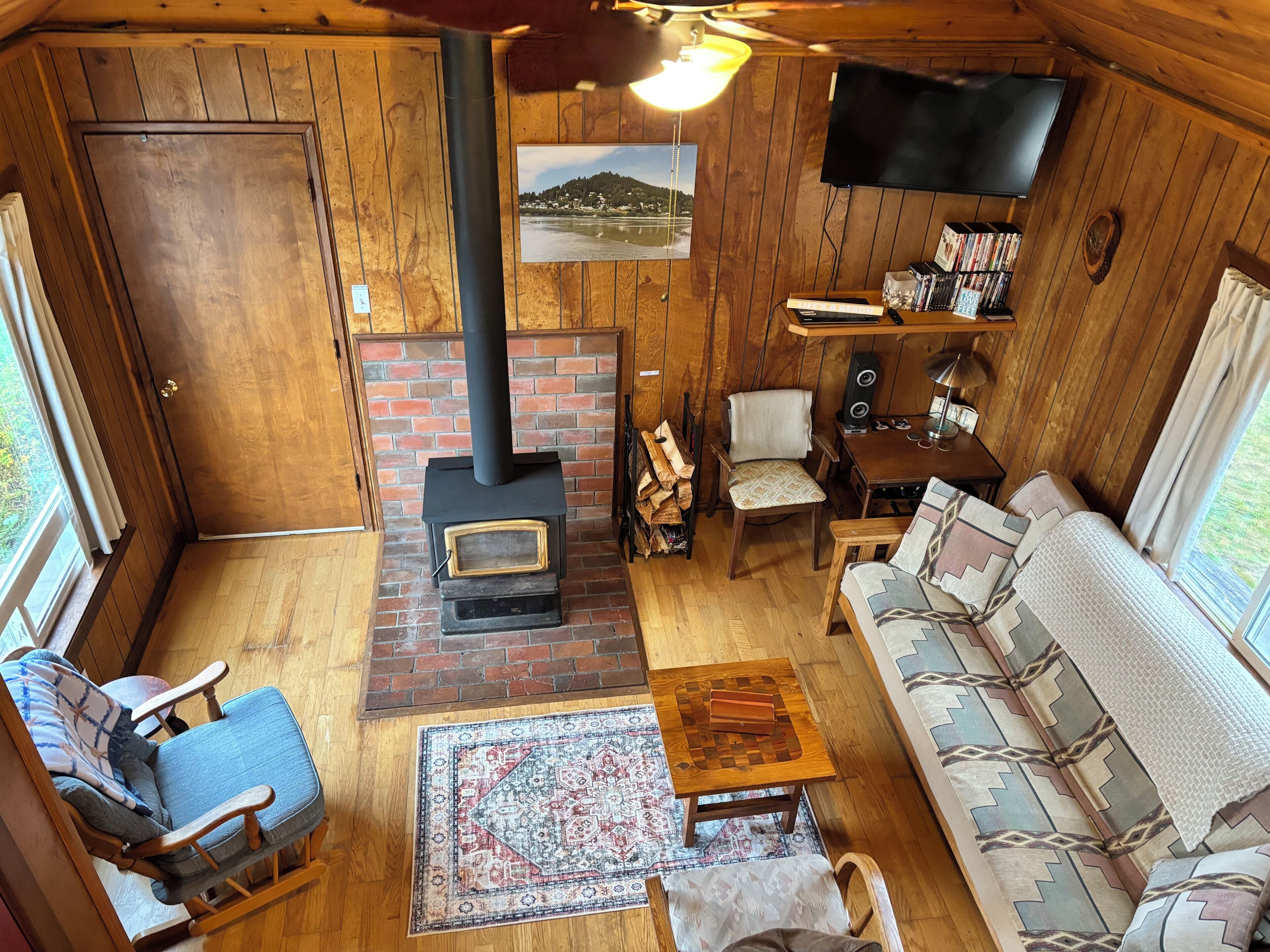 A cozy cabin interior with a fireplace, wooden walls, a sofa, and a television.