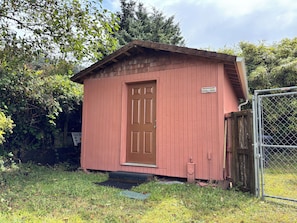 Ein kleines, eingeschossiges Gartenhaus mit brauner Tür und einer kleinen Veranda.