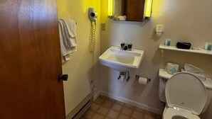 Casa de banho padrão de hotel, com lavatório, sanita e espelho sobre o lavatório.