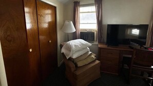 Quarto de hotel com guarda-roupa de madeira, uma mesa de trabalho com televisão, uma cadeira e uma luminária.