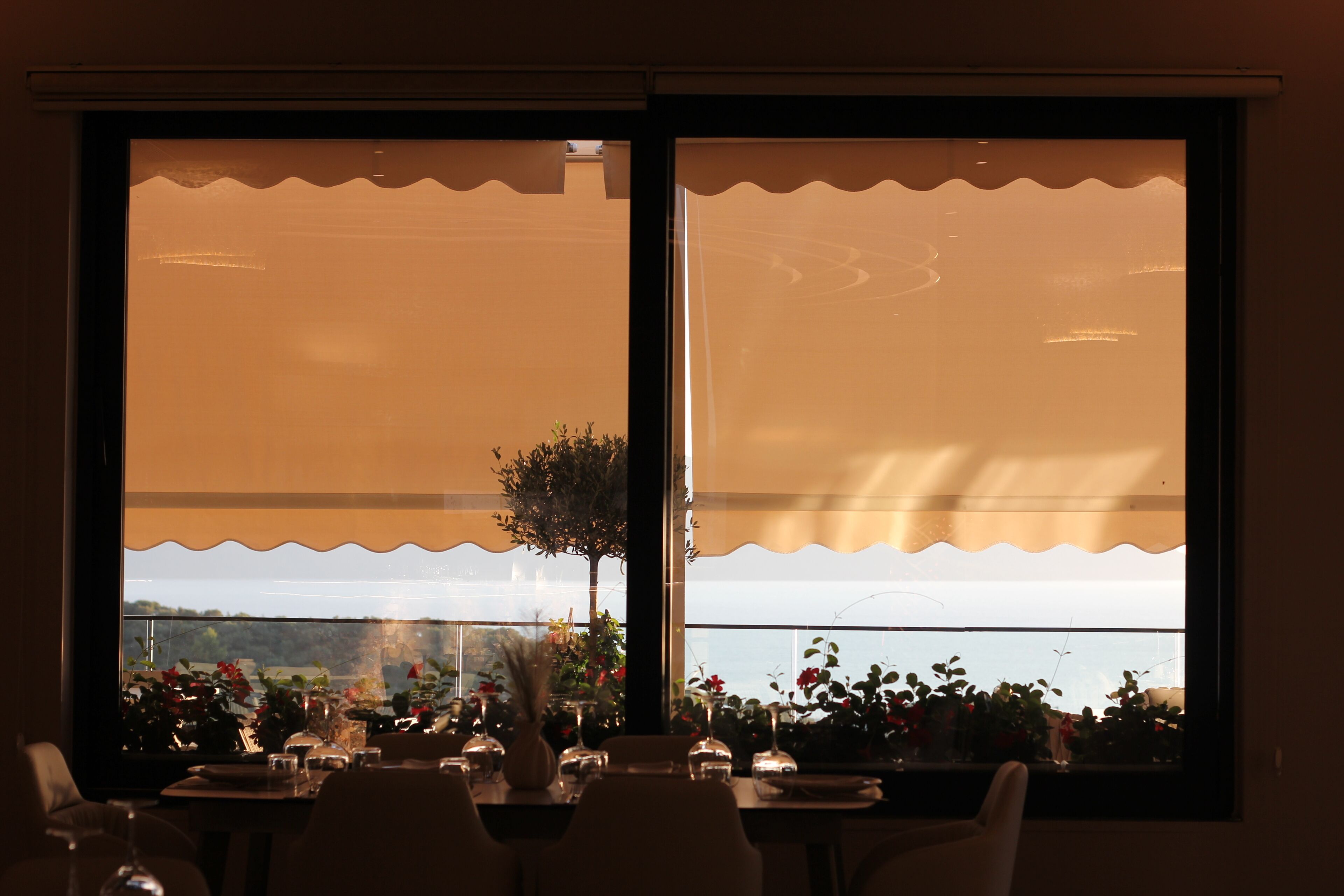 Un coin repas avec une table dressée pour deux personnes, une fenêtre donnant sur la mer et une plante placée sur le rebord de la fenêtre.