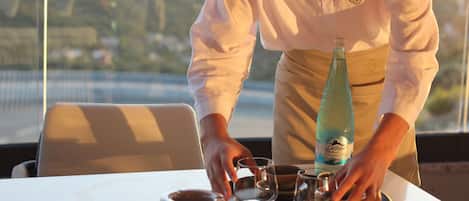 A person setting a table with a bottle, glasses, and a bowl.