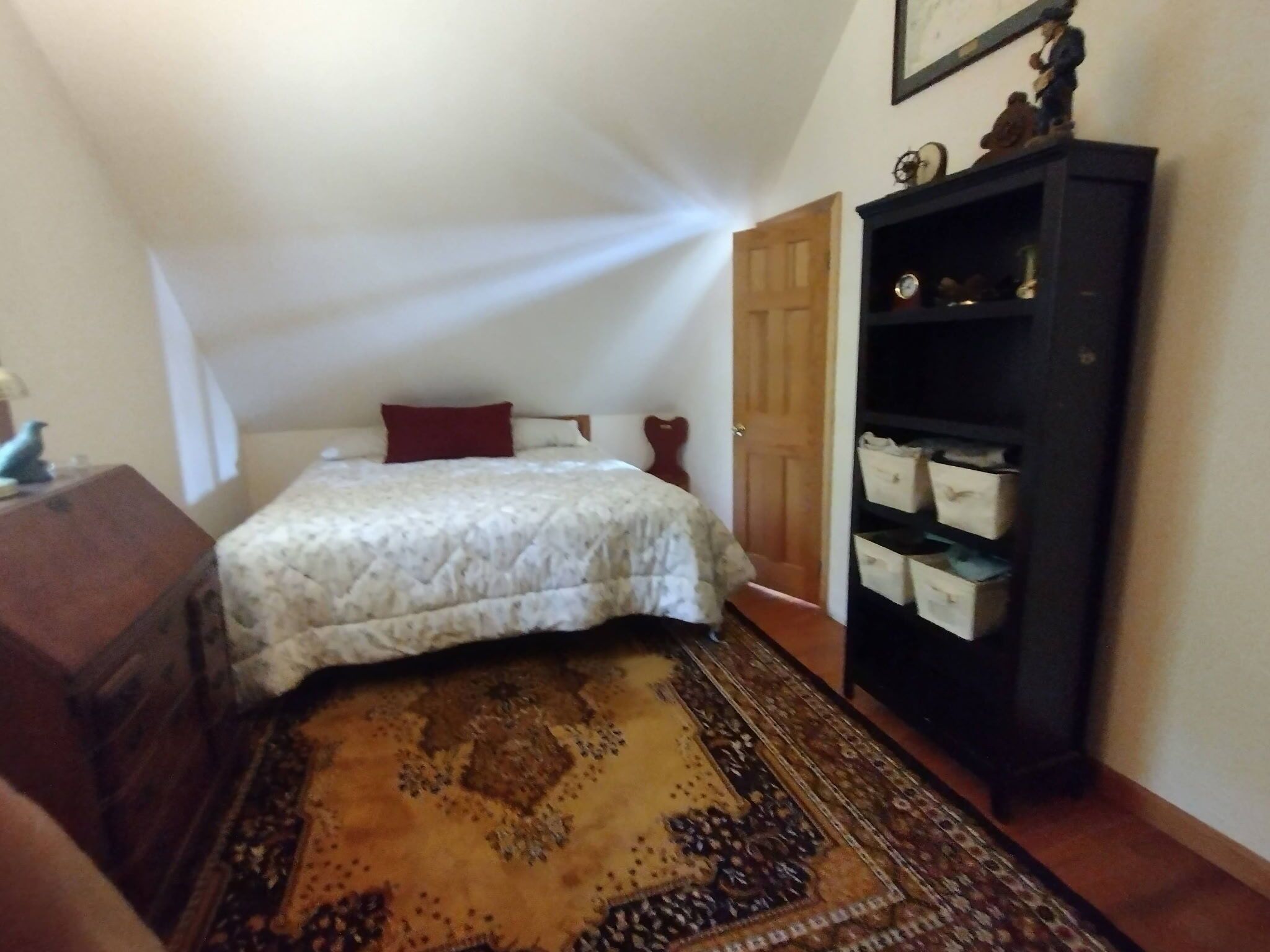 Een slaapkamer met een bed, een houten dressoir, een boekenkast en een kamerkleed met dessin.