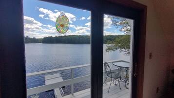 Vista de um quarto com porta para um deck com vista para um lago, com mesa e cadeiras no deck.
