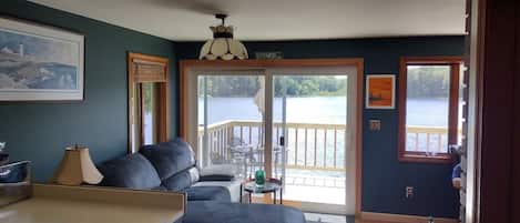 Quarto com sofá, mesa, luminária, pintura e vista para um lago através de uma porta de vidro.