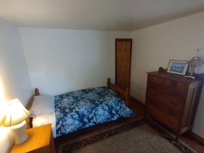 Un dormitorio pequeño con cama, cómoda, mesita de noche y lámpara.