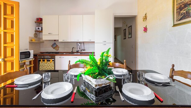A dining area with a table set for four, a kitchen in the background, and a hallway leading to another room. - Villetta Lea by BarbarHouse (San Pietro in Bevagna)
