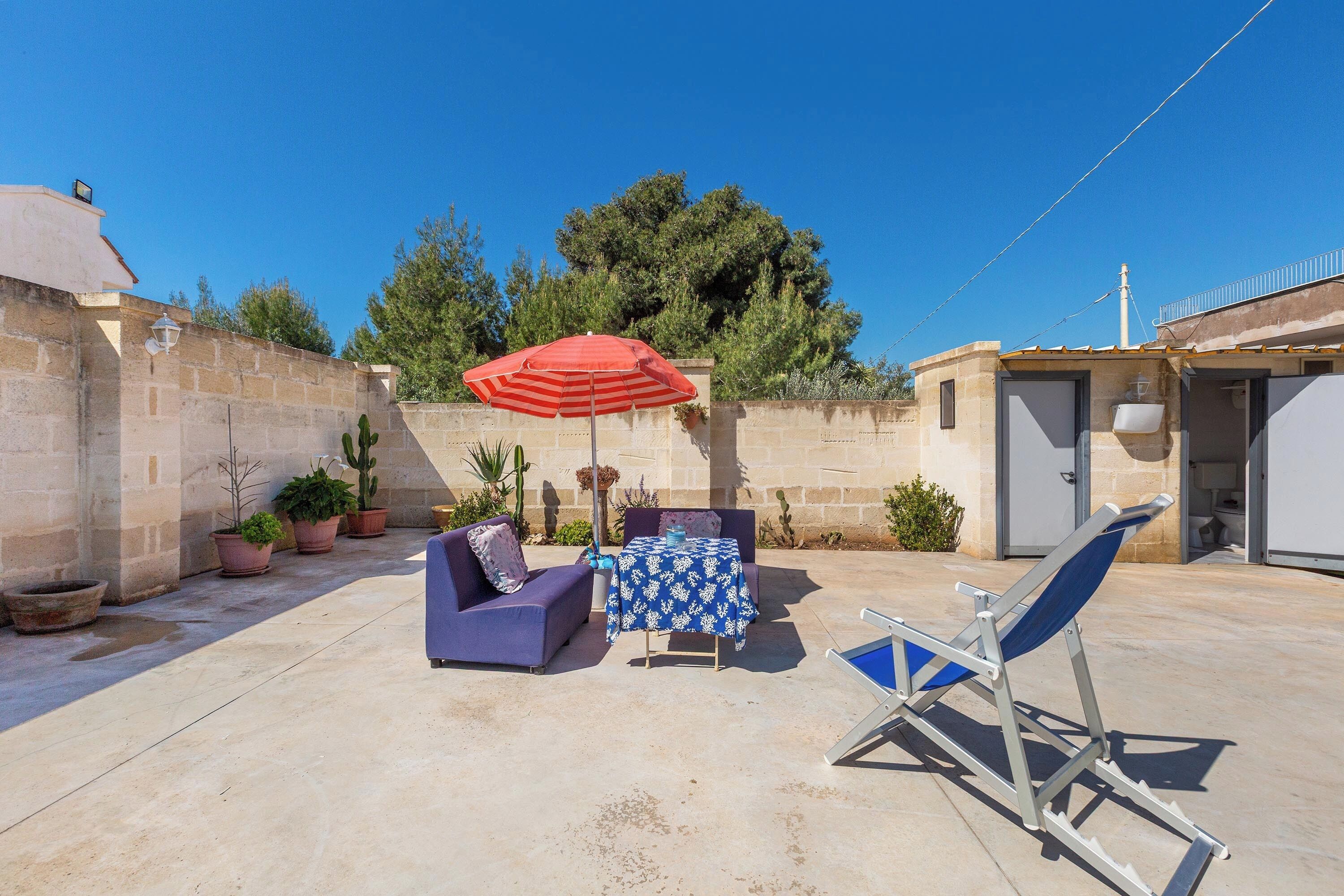Eine Terrasse mit Tisch, Stuhl, Sonnenschirm und Topfpflanzen.
