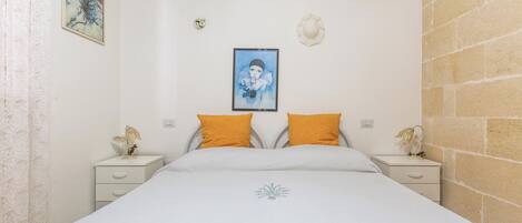 A bedroom with a bed, two nightstands, a wall-mounted air conditioner, and a single artwork.