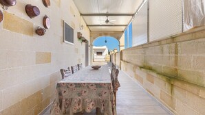 A covered outdoor dining area with a long table and chairs, a ceiling fan, and a view of a building in the background. - Villetta Lea by BarbarHouse (San Pietro in Bevagna)