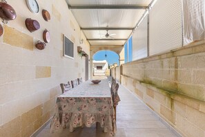 A covered outdoor dining area with a long table and chairs, a ceiling fan, and a view of a building in the background. - Villetta Lea by BarbarHouse (San Pietro in Bevagna)