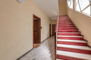 A staircase with red steps leading to an upper floor, a tiled floor, and a door at the bottom of the stairs. - Due Passi dal Vaticano by BarbarHouse (Roma)