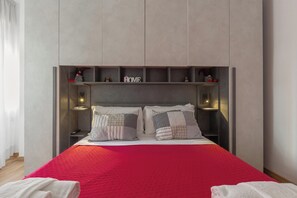 Un dormitorio moderno con cama, almohadas, una colcha roja y estantes empotrados con objetos decorativos.
