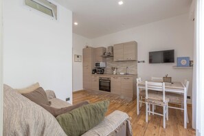 A modern living room with a sofa, a dining table with chairs, and a kitchen area with appliances and cabinets. - Due Passi dal Vaticano by BarbarHouse (Roma)