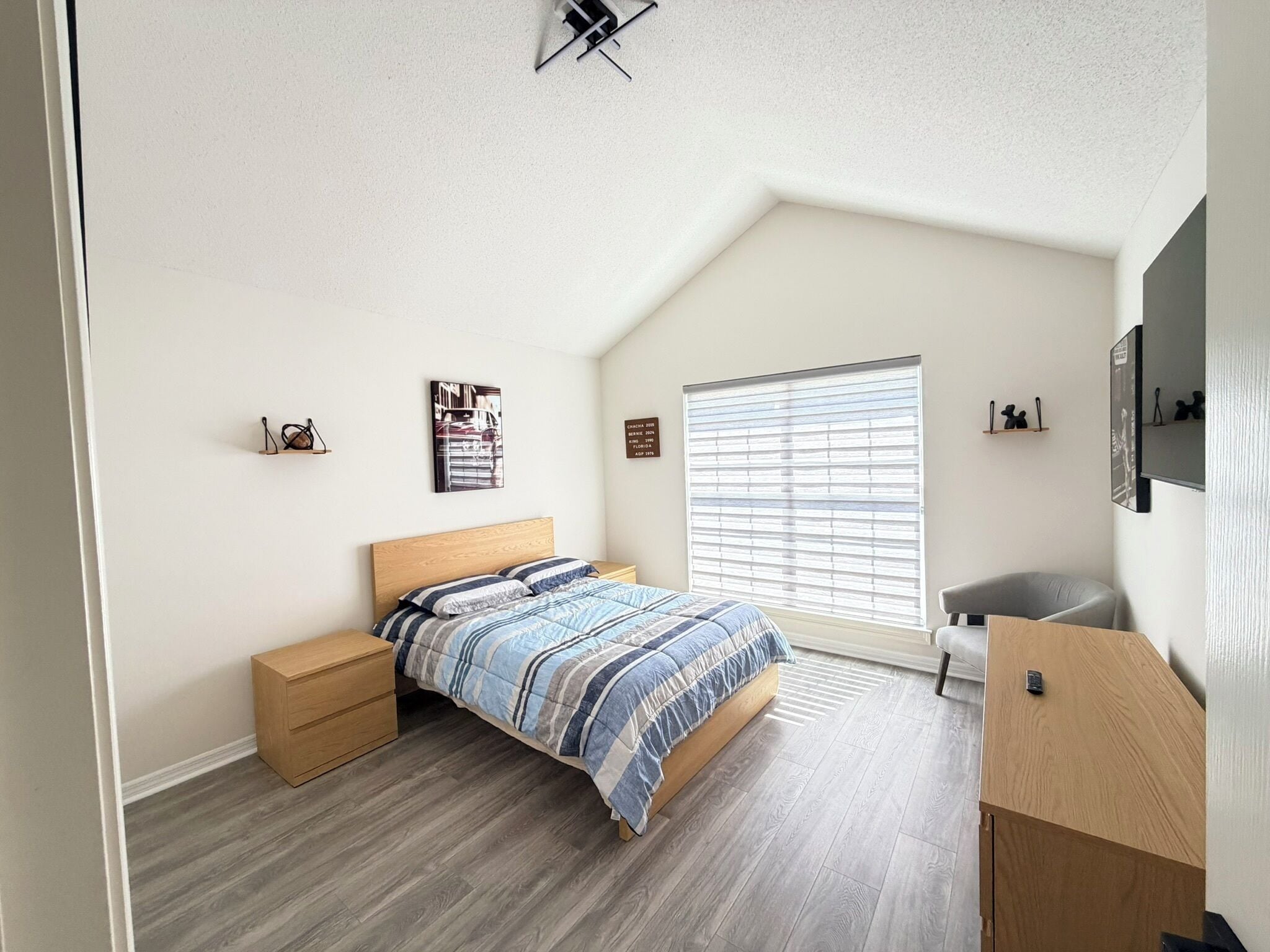 A bedroom with a bed, a nightstand, a desk, a window with blinds, and wall decorations.