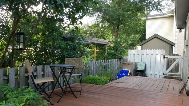 A wooden deck with a table and chairs, surrounded by a wooden fence and greenery. - Otto Street, Osgoode. (osgoode)