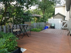 A wooden deck with a table and chairs, surrounded by a wooden fence and greenery.