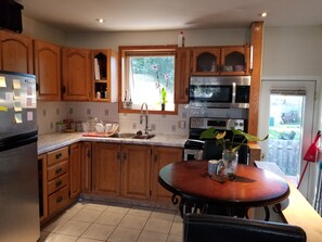 Eine Küche mit Holzschränken, einem Edelstahlkühlschrank, einer Mikrowelle, einem Backofen und einem Esstisch mit Stühlen.