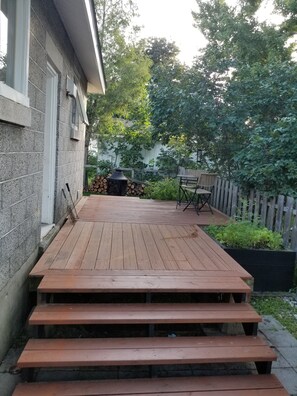 A wooden deck with steps leading to a patio area, a barbecue grill, and a wooden fence. - Otto Street, Osgoode. (osgoode)