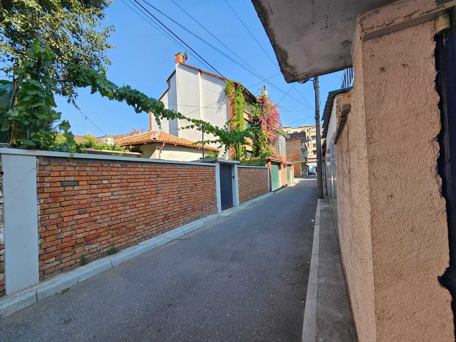 Une rue étroite, bordée d’un côté par un mur de briques et de l’autre par un bâtiment dont le toit est recouvert de tuiles.