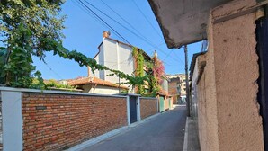 Une rue étroite, bordée d’un côté par un mur de briques et de l’autre par un bâtiment dont le toit est recouvert de tuiles.