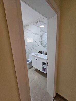 A bathroom with a marble wall, a white sink, and a toilet.