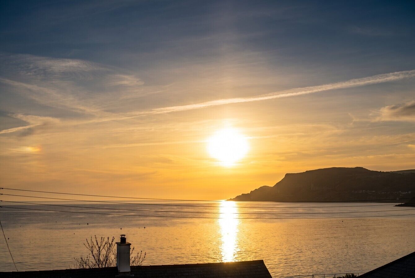 A sunset over a calm body of water with a distant landmass and a chimney in the foreground.