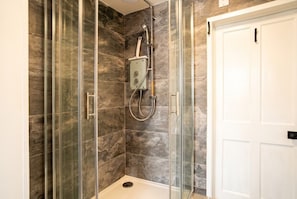 A shower with glass doors, a white door, and a marble wall. - Coastal Studio · Sleeps 2 · Walk to Cushendall Beach & Glens (Cushendall)