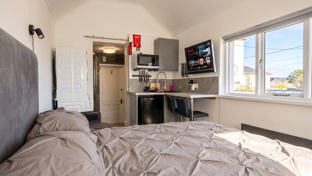 Ein kleines Schlafzimmer mit Bett, einer Küchenzeile, einem Fernseher und einem Fenster.