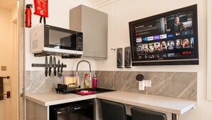 Eine kompakte Küchenzeile mit Mikrowelle, Spüle und einem Flachbildfernseher, der eine Streaming-Dienstanwendung anzeigt.