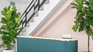 Ein Empfangsschalter mit Datumsanzeige, flankiert von Blumentöpfen, in einem modernen Gebäude mit Treppe.
