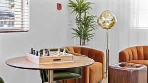 A room with a chessboard on a table, two armchairs, a floor lamp, and a potted plant.