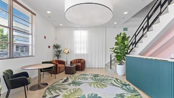 A modern lobby with a round table, seating, a staircase, and a large plant.