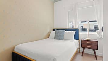 Un dormitorio con cama, mesita de noche, ventana con cortinas y vistas al exterior.