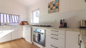 A kitchen with white cabinets, a stove, a coffee maker, and a window with blinds. - Tranquil 3-bedroom house in charming Onrusrivier for your getaway (Onrusrivier)