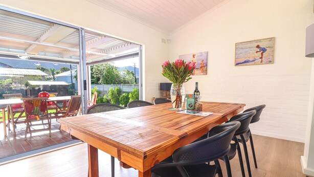 A dining area with a wooden table, black chairs, a vase with flowers, and a painting on the wall. - Tranquil 3-bedroom house in charming Onrusrivier for your getaway (Onrusrivier)