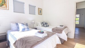 A hotel room with two beds, a nightstand, a lamp, and a door leading to another room. - Tranquil 3-bedroom house in charming Onrusrivier for your getaway (Onrusrivier)