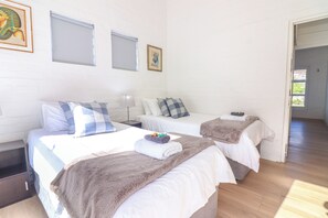 A hotel room with two beds, a nightstand, a lamp, and a door leading to another room. - Tranquil 3-bedroom house in charming Onrusrivier for your getaway (Onrusrivier)