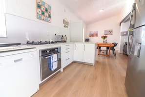 A modern kitchen with white cabinetry, a built-in oven, and a dining area with a wooden table. - Tranquil 3-bedroom house in charming Onrusrivier for your getaway (Onrusrivier)
