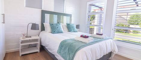 A bedroom with a bed, nightstand, and window with blinds.