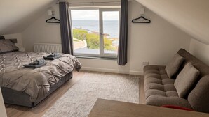 Une chambre à coucher avec un lit, un canapé, une fenêtre donnant sur la mer et un radiateur.