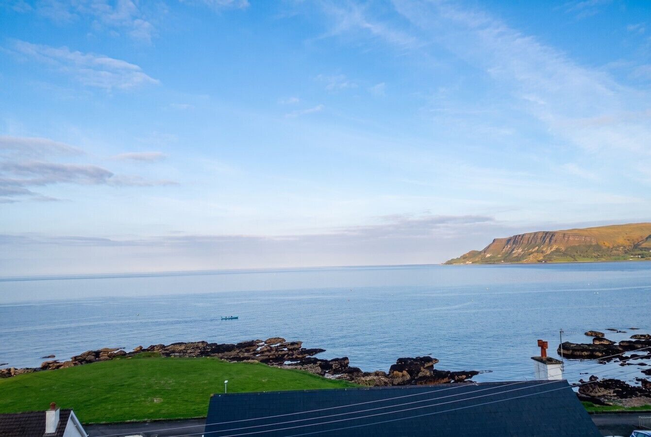 A coastal landscape with a view of the sea, rocky outcrops, and a grassy area.