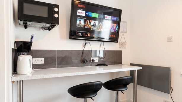Een kitchenette met een magnetron, een flatscreen televisie boven de aanrecht gemonteerd, en twee barkrukken.