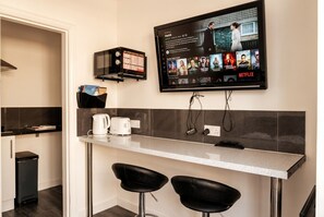 A modern kitchen with a flat-screen TV mounted above a bar area, a coffee maker, and two black bar stools. - Coastal Studio Apartments 1-Bed Flat Sleeps 3 · Walk to Cushendall Beach (Cushendall)