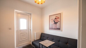 Een kamer met een donkere bank, een klein tafeltje, een radiator, een deur en een lijst met een afbeelding aan de muur.