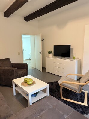 Ein stilvolles Wohnzimmer mit einer Couch, einem Couchtisch mit Äpfeln, einem Fernseher auf einem weißen Schrank und einem flauschigen Teppich.